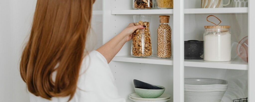 Femme au cheveux bruns-roux qui organise des aliments dans des contenants situés sur des étagères de cuisine.