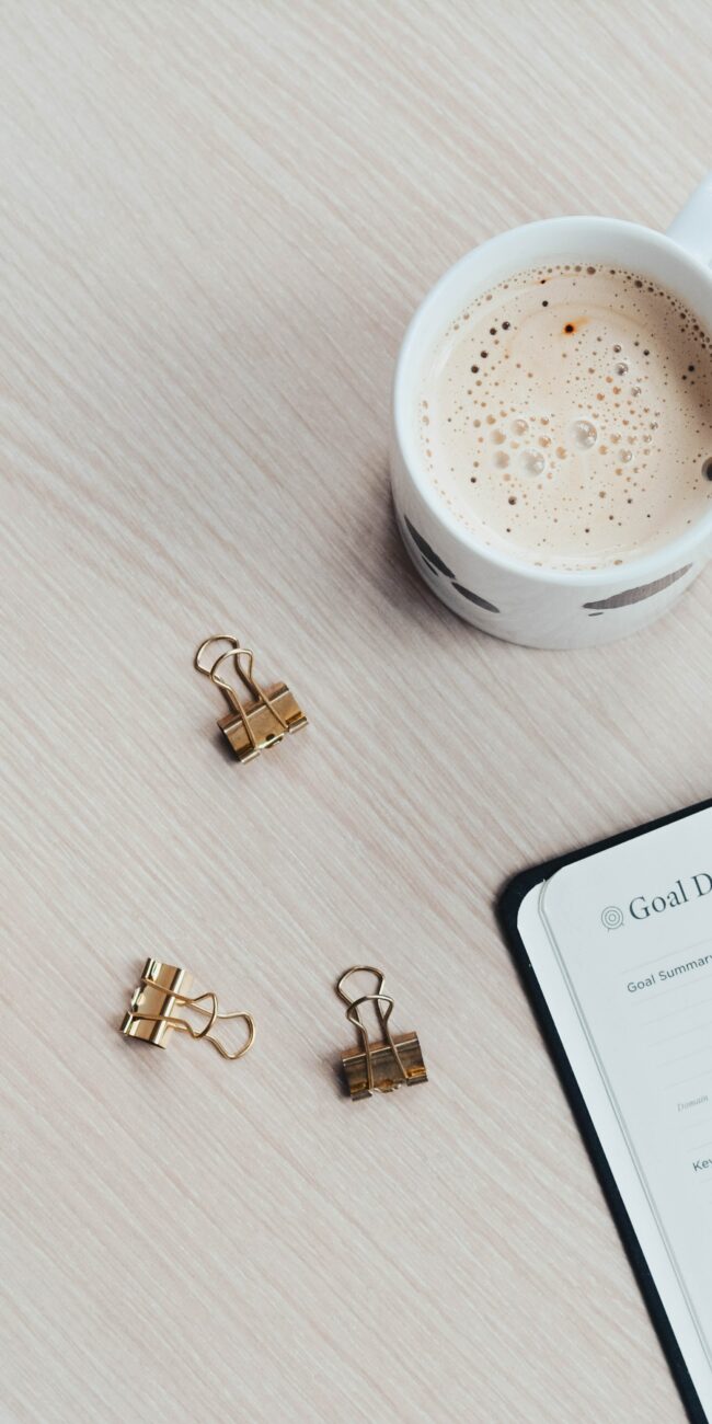 Agenda pour écrire ses objectifs. On voit une tasse de café, une montre et des pinces à clips.