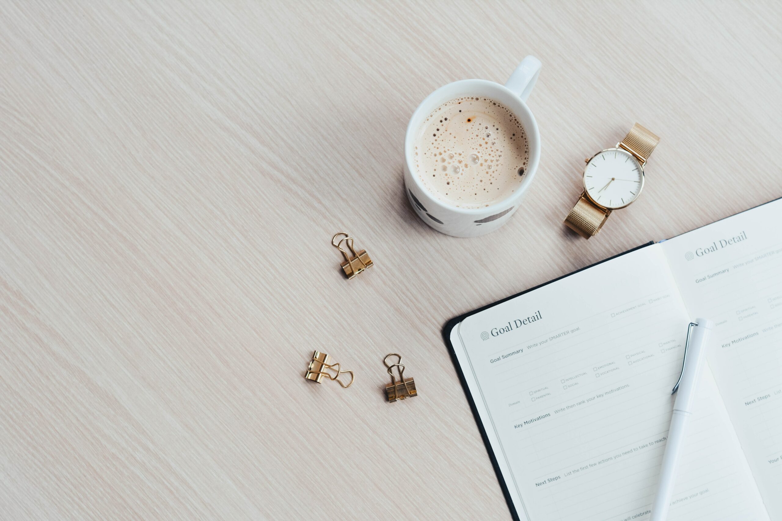 Agenda pour écrire ses objectifs. On voit une tasse de café, une montre et des pinces à clips.