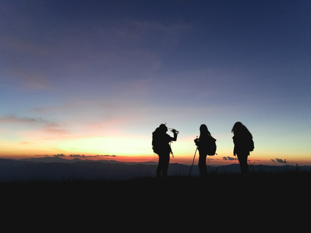 Groupe de trois personnes en randonnée lors d'un couché de soleil l'été. 