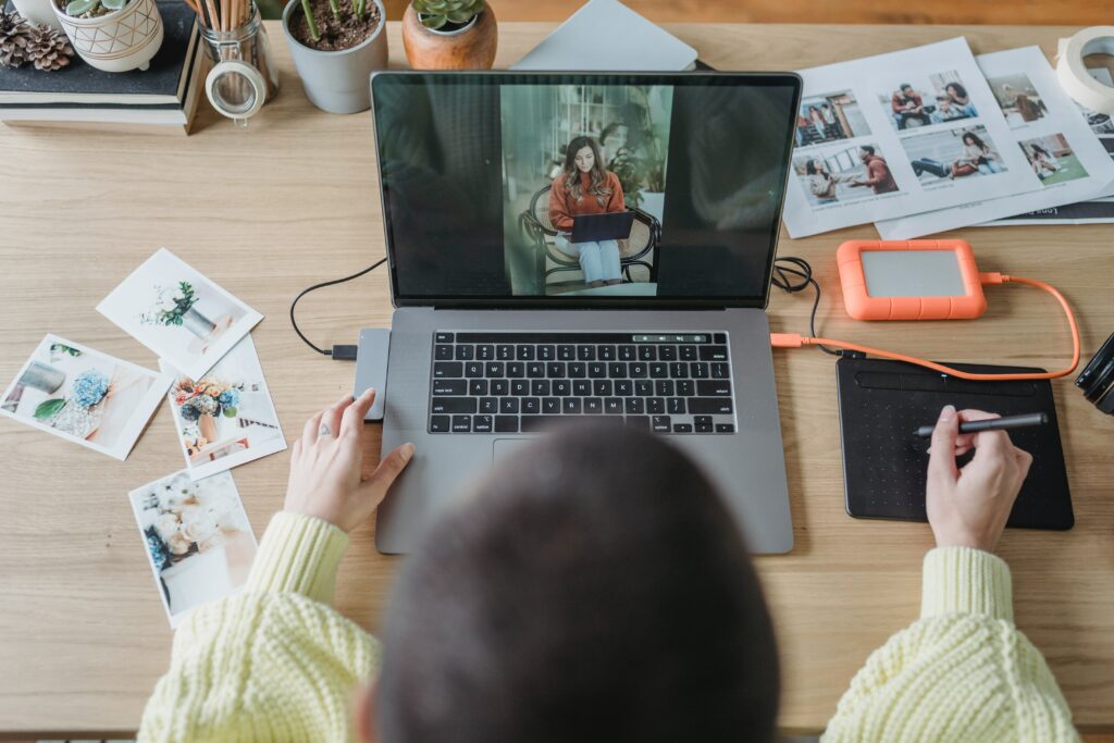 Femme aux cheveux courts assise devant son ordinateur et qui fait la sauvegarde de ses photos sur un disque dur externe branché à son ordinateur portable.