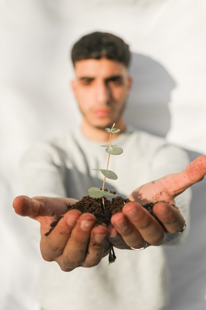 Écologie. Un jeune homme aux cheveux courts et bruns foncés tient une pousse de plante avec de la terre dans ses mains.