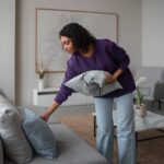 Une femme ajuste des coussins dans un salon lumineux et épuré, illustrant une étape clé de la valorisation immobilière avant la vente d’une propriété.