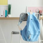 Sac à dos bleu accroché à une chaise devant un bureau organisé, illustrant un espace de travail idéal pour bien préparer la rentrée scolaire.
