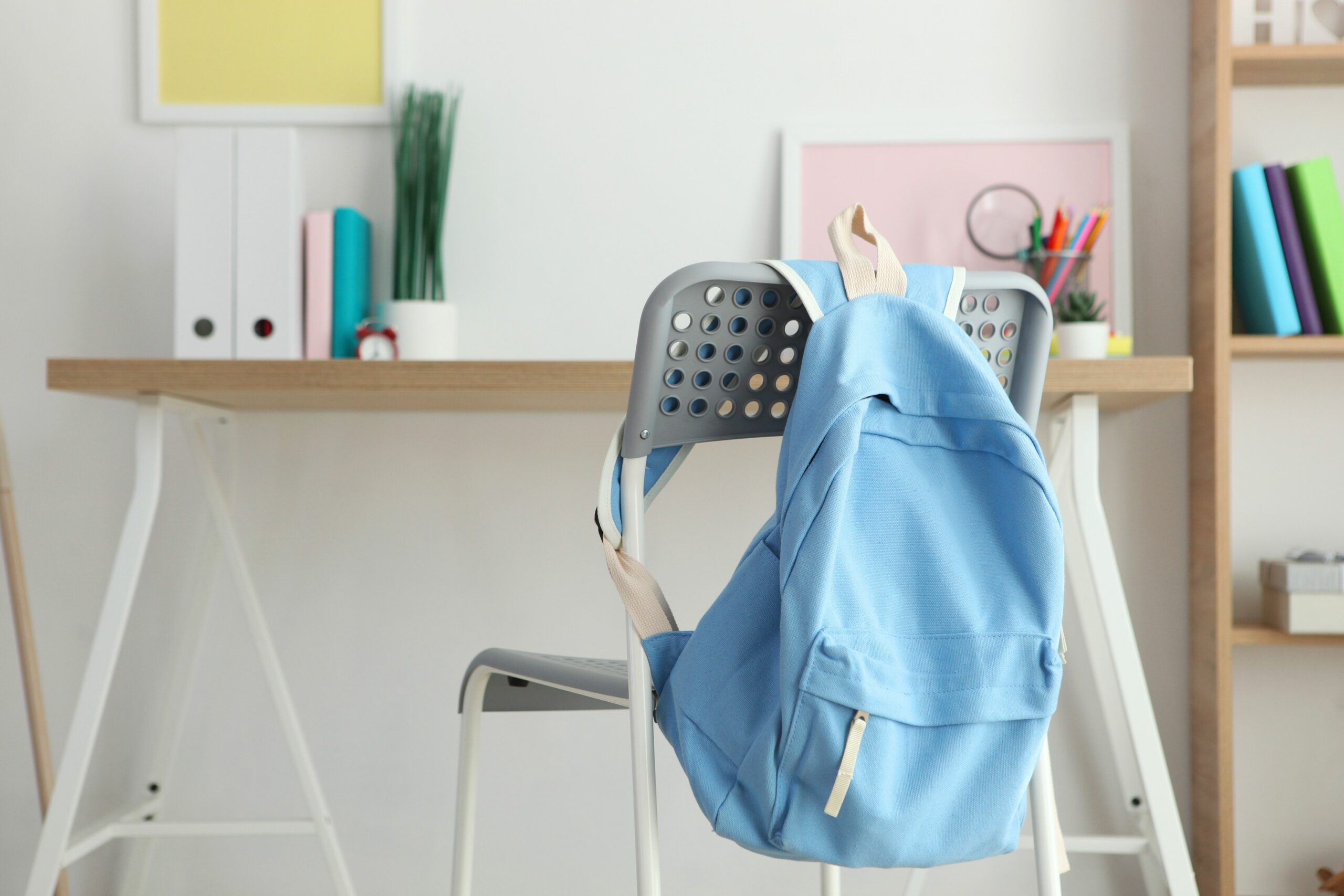 Sac à dos bleu accroché à une chaise devant un bureau organisé, illustrant un espace de travail idéal pour bien préparer la rentrée scolaire.