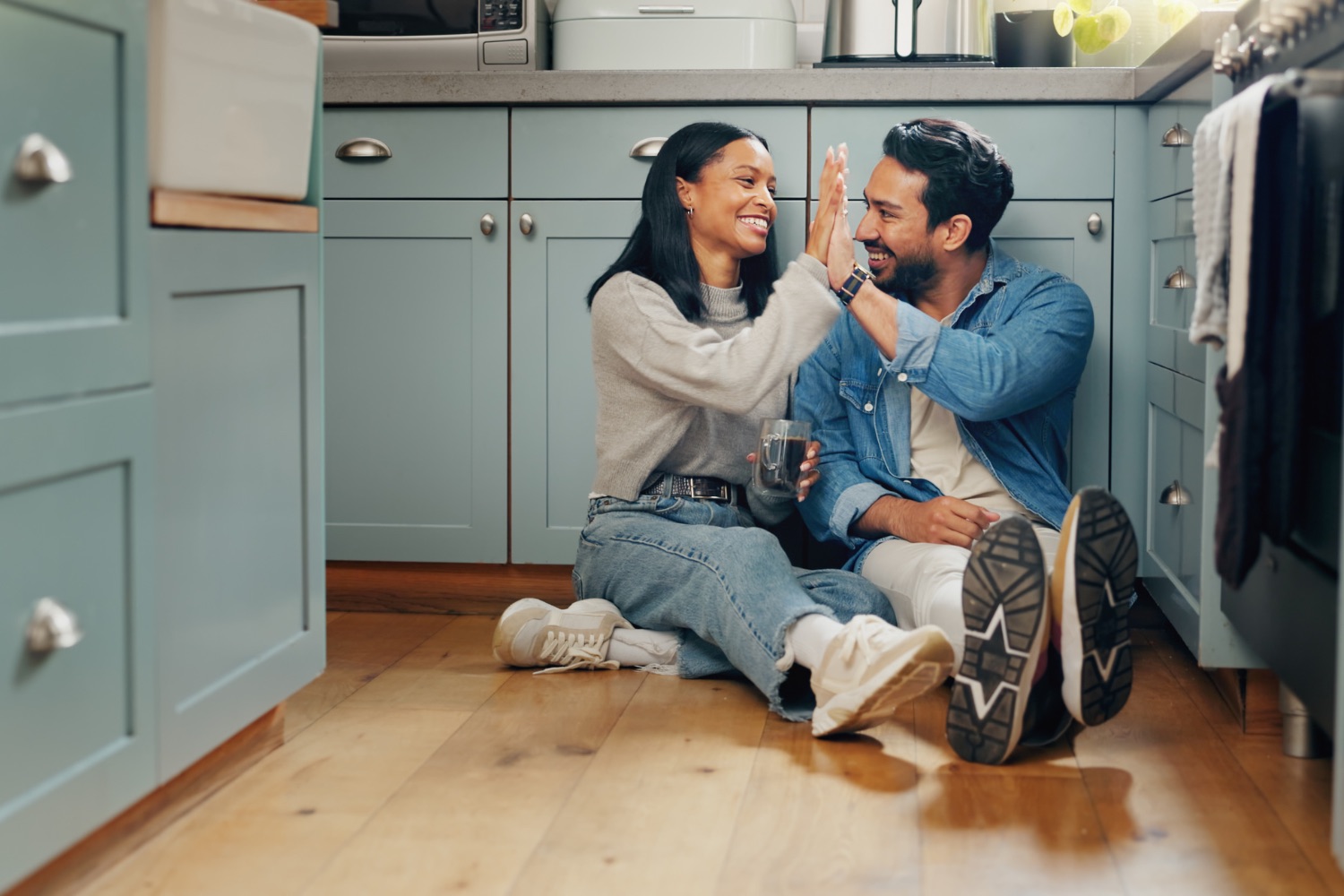 Couple souriant assis sur le plancher de la cuisine, se tapant dans la main dans un moment complice.
