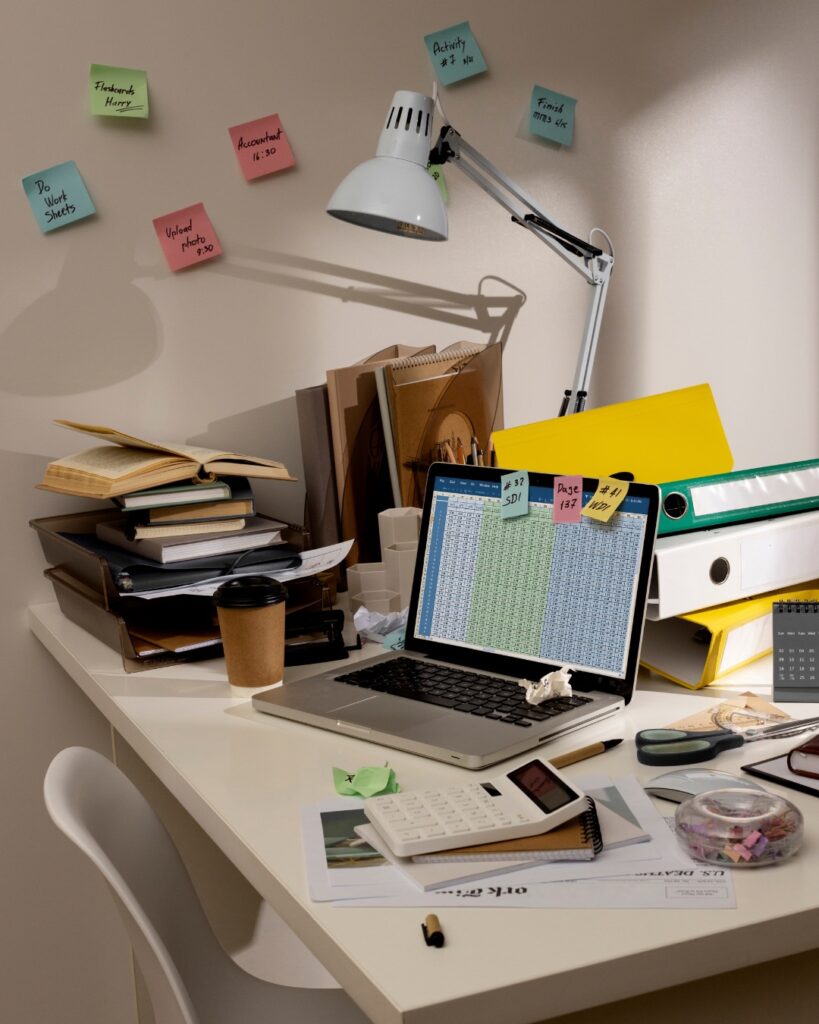 Espace de travail encombré avec des dossiers, des notes autocollantes colorées et divers objets éparpillés sur le bureau.