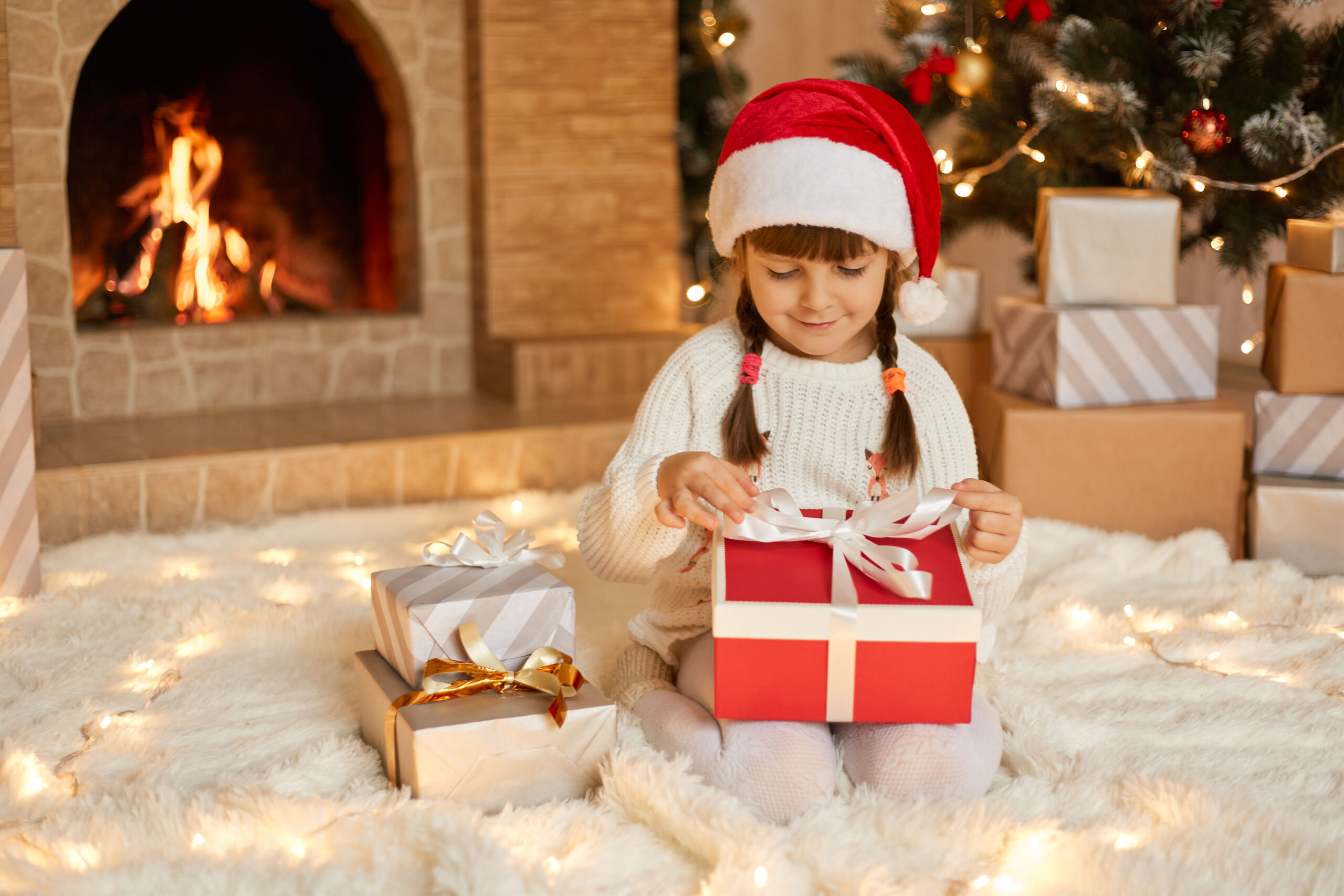Petite fille assise devant un foyer décoré pour Noël, ouvrant un cadeau, une scène qui illustre l’importance du désencombrement avant l’arrivée des Fêtes.