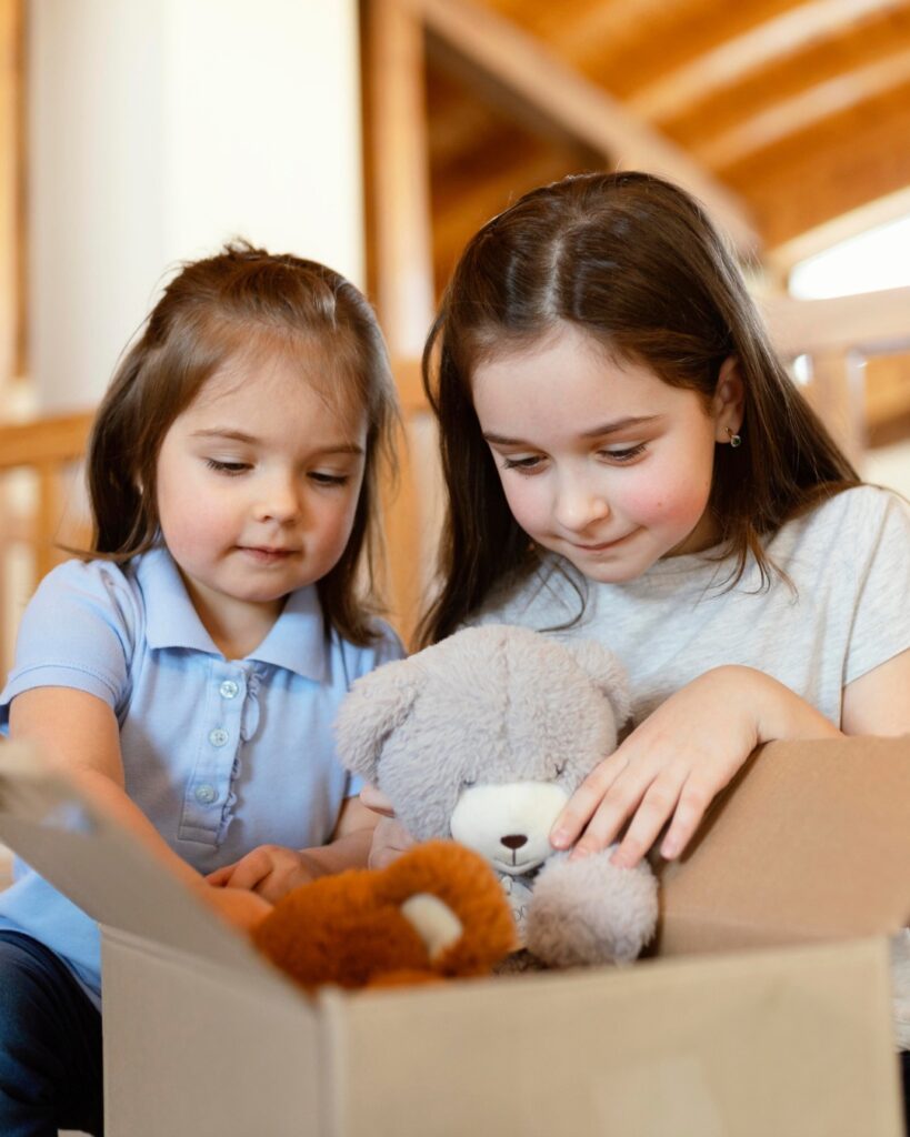 Deux jeunes filles qui placent des peluches dans une boîte de dons, un beau geste de désencombrement fait en famille avant Noël.
