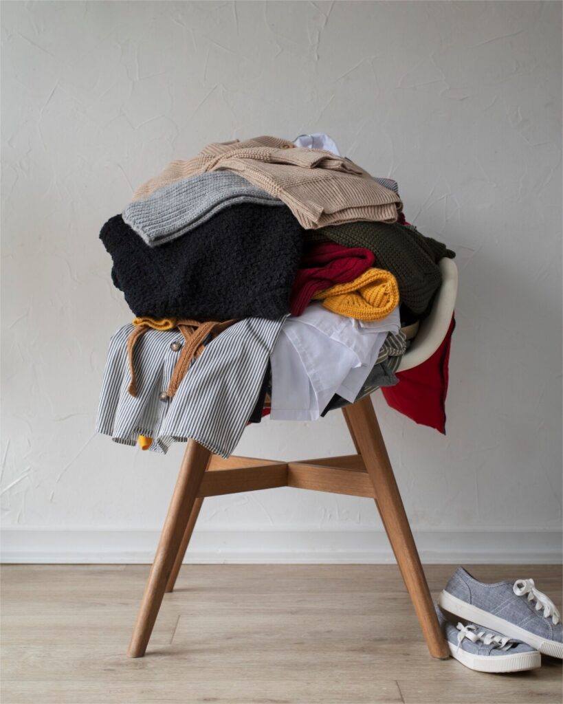 Pile de vêtements accumulés sur une chaise dans une chambre, représentant le quotidien de nombreux couples et l’importance de désencombrer pour réduire la charge mentale.
