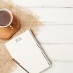 Cahier ouvert avec l’année 2026 écrite à la main, accompagné d’une tasse de thé, évoquant la réflexion, les intentions et l’alignement pour la nouvelle année.