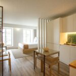 Studio lumineux bien organisé avec cuisine minimaliste, coin repas, espace de travail et lit séparé par une cloison, illustrant l’optimisation d’un petit espace de condo.