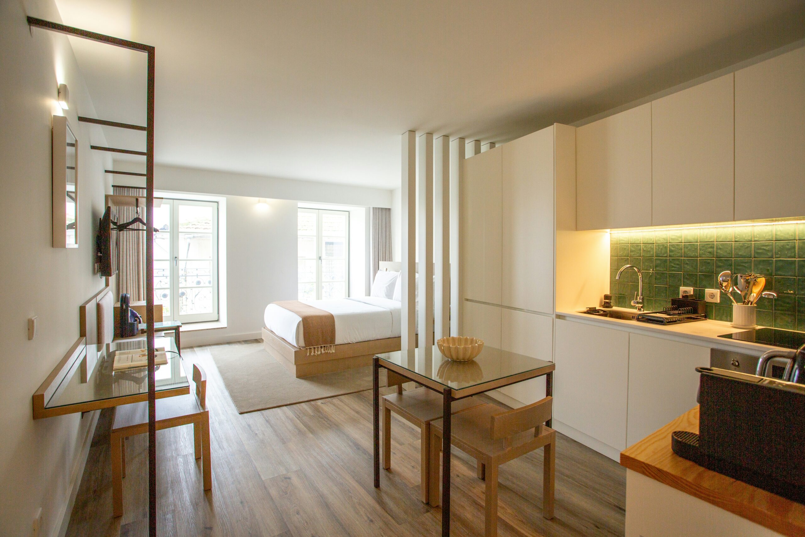 Studio lumineux bien organisé avec cuisine minimaliste, coin repas, espace de travail et lit séparé par une cloison, illustrant l’optimisation d’un petit espace de condo.