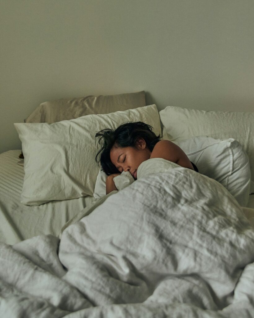 Personne reposant dans un lit aux draps blancs, symbolisant le besoin de calme, de repos et de bien-être pendant une période de transition ou de changement de vie.