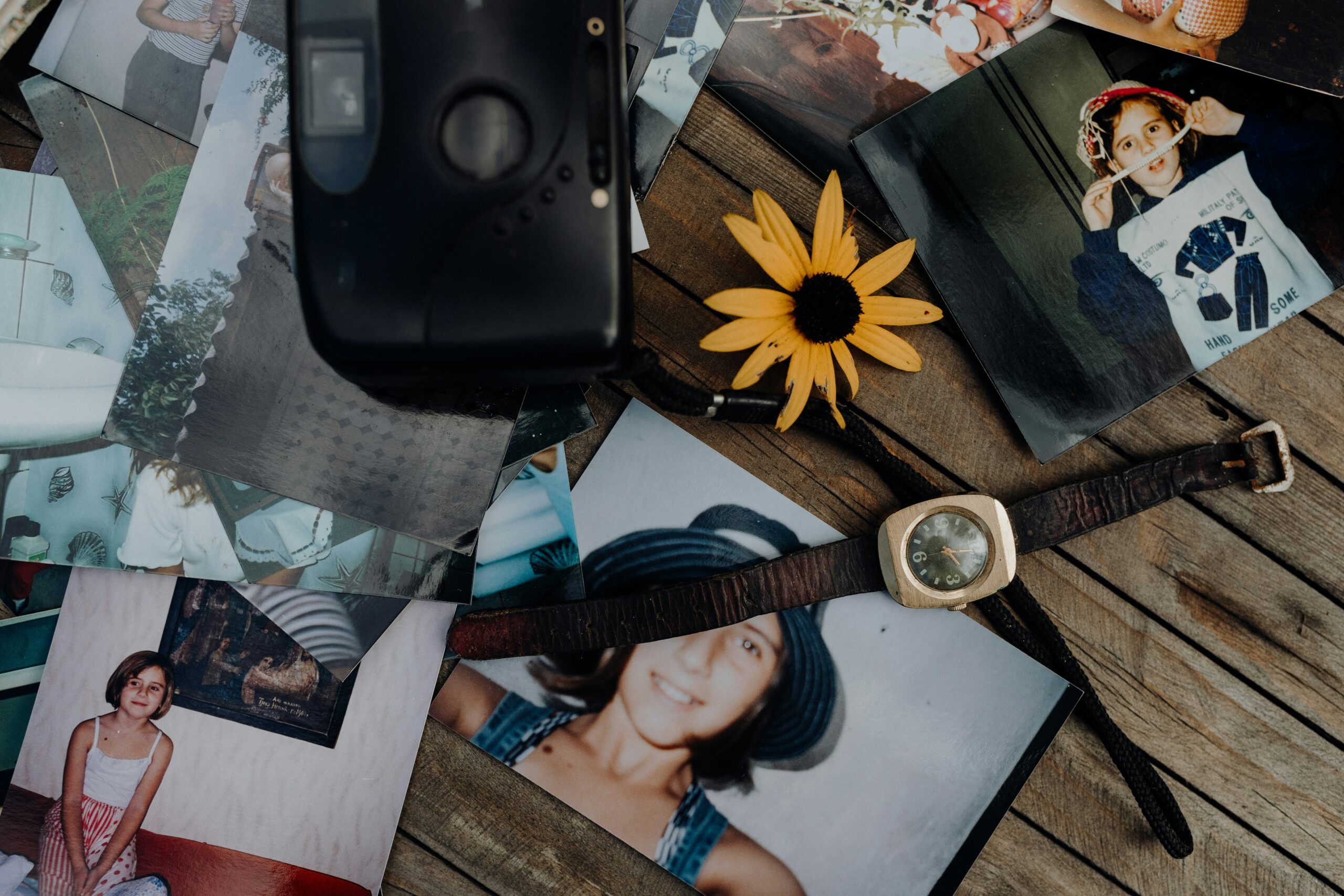 Vieilles photographies, montre, appareil photo et objets souvenirs disposés sur une table en bois, représentant l'attachement aux objets, les souvenirs de famille et les moments précieux qui marquent une vie.